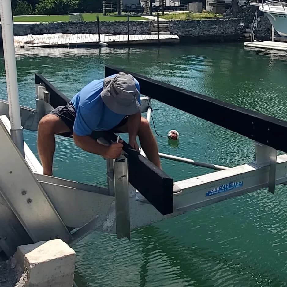 A worker adjusting a black boat lift bunk at the dock