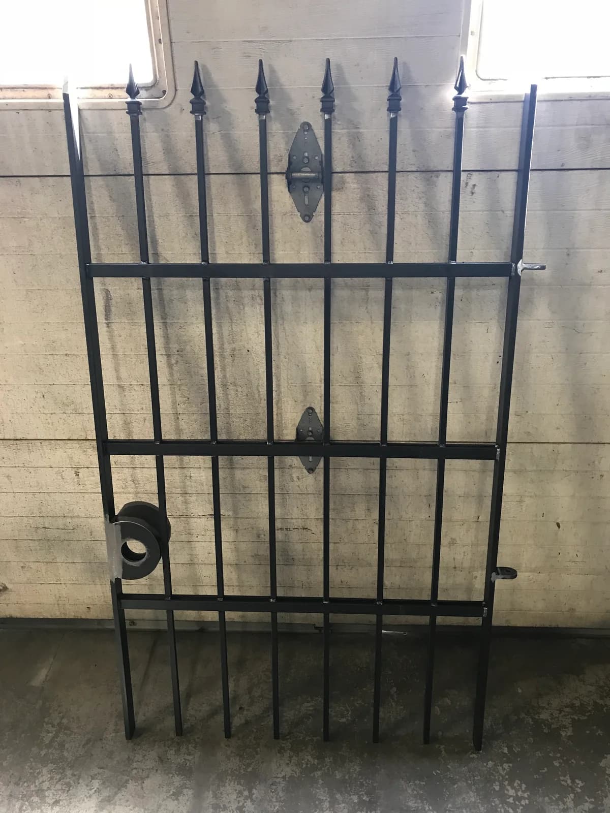 Dark metal gate with pointed finials, hinges, and a latch opening